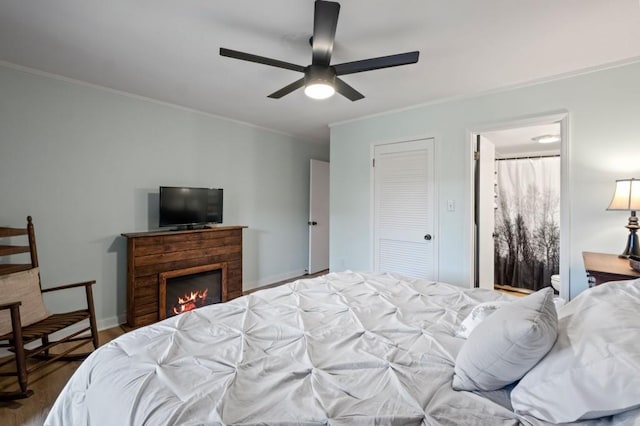 bedroom with ornamental molding, dark wood-type flooring, a ceiling fan, a lit fireplace, and baseboards