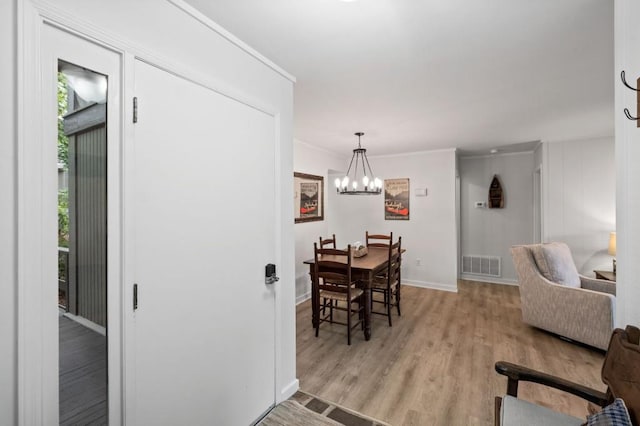 dining space with crown molding, visible vents, light wood-style floors, a chandelier, and baseboards