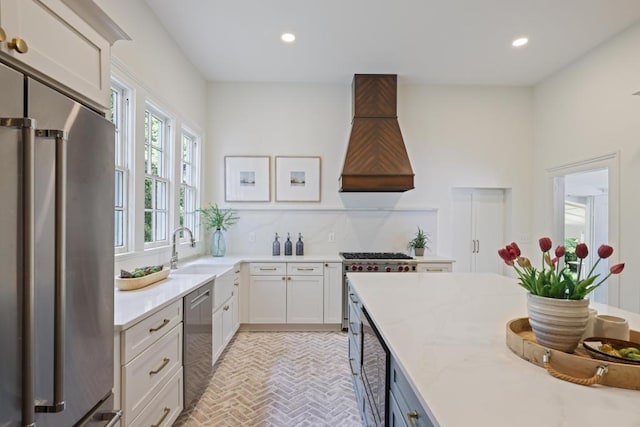 kitchen featuring stainless steel appliances, premium range hood, brick patterned floors, recessed lighting, and a sink