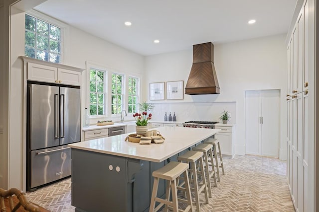 kitchen with stainless steel appliances, premium range hood, brick floors, recessed lighting, and light countertops