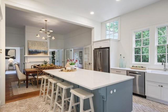 kitchen featuring stainless steel appliances, a center island, white cabinetry, a chandelier, and light countertops