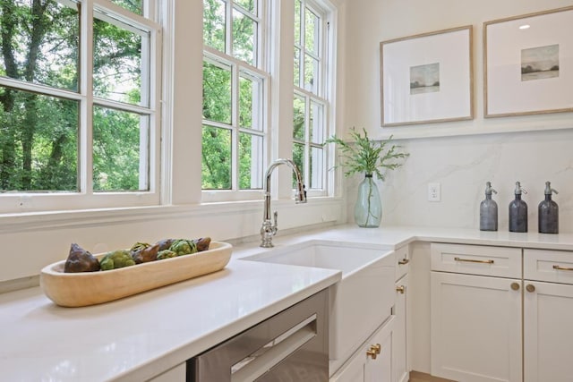 kitchen featuring stainless steel dishwasher, decorative backsplash, a sink, and light countertops