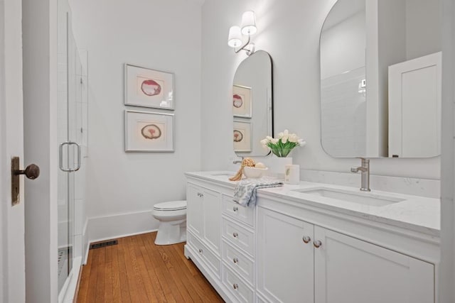 full bath with a stall shower, double vanity, wood finished floors, toilet, and baseboards