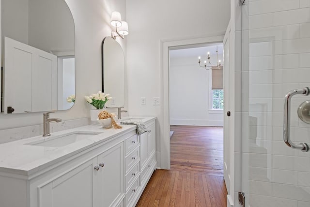 full bathroom featuring hardwood / wood-style flooring, double vanity, an enclosed shower, a chandelier, and baseboards