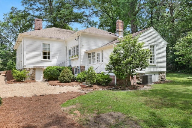 back of house featuring a chimney, a lawn, central AC unit, and a shingled roof