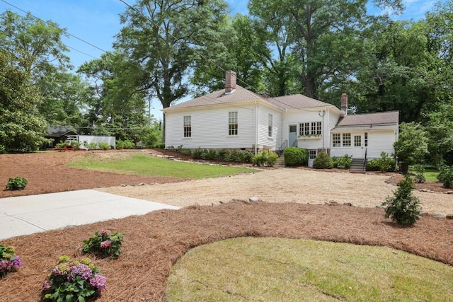 view of front facade featuring a chimney, a front lawn, and dirt driveway