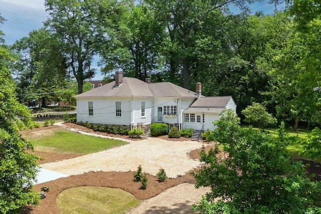 view of front of property featuring a chimney, driveway, and view of wooded area