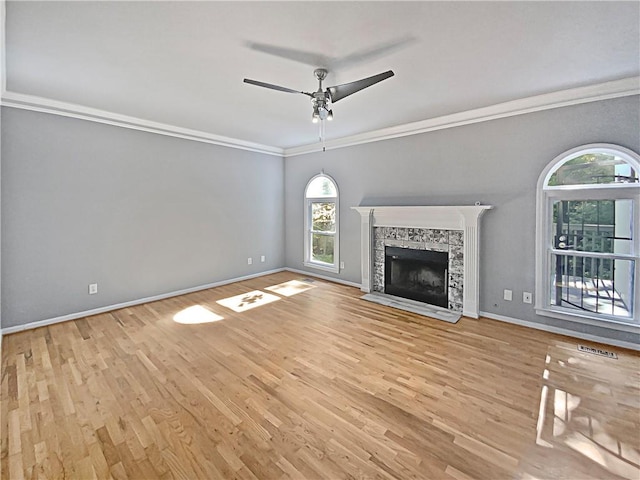 unfurnished living room featuring ceiling fan, a stone fireplace, ornamental molding, and light hardwood / wood-style floors