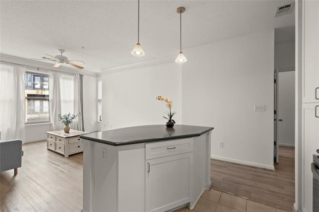 kitchen with visible vents, dark countertops, a center island, a textured ceiling, and pendant lighting