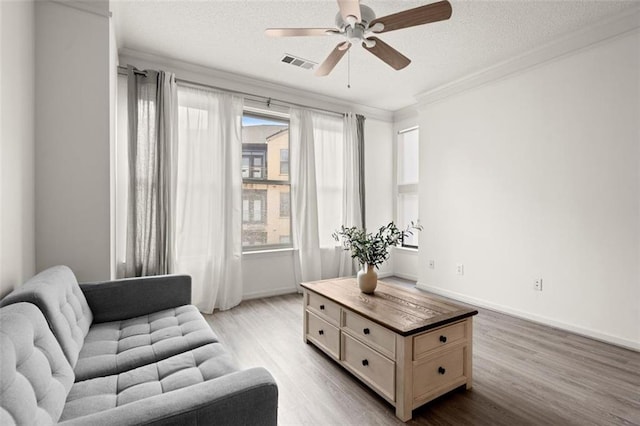 living area featuring a textured ceiling, visible vents, wood finished floors, and ornamental molding