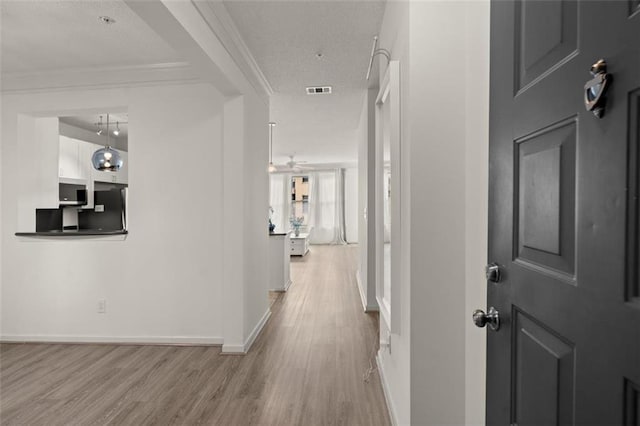 hall with ornamental molding, light wood-type flooring, a textured ceiling, and baseboards