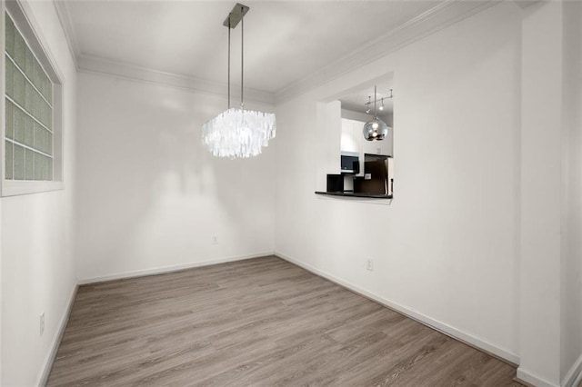 unfurnished dining area with ornamental molding, an inviting chandelier, baseboards, and wood finished floors