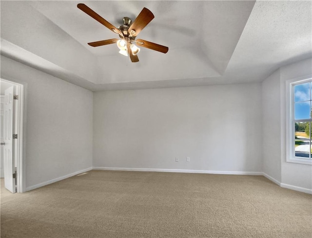 unfurnished room with a textured ceiling, light colored carpet, ceiling fan, and a raised ceiling