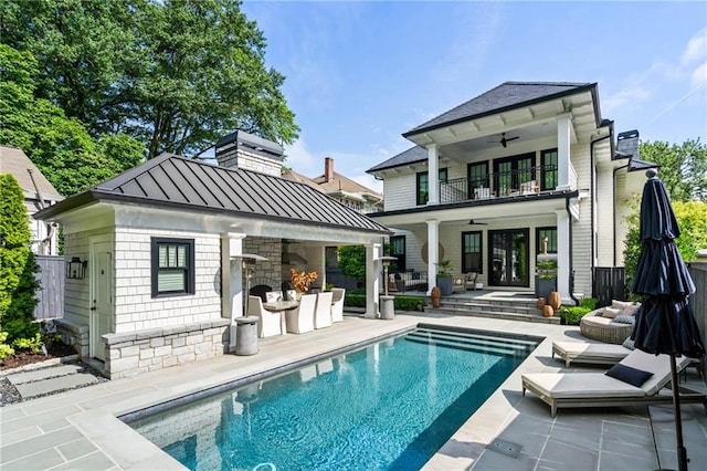 back of property featuring ceiling fan, an outdoor structure, exterior fireplace, a balcony, and a patio area