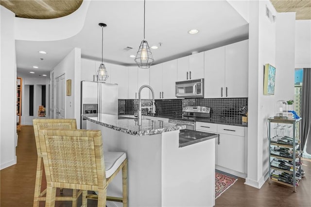 kitchen featuring backsplash, pendant lighting, dark wood-style flooring, stainless steel appliances, and a kitchen island with sink