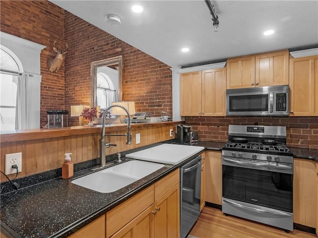 kitchen with light wood-style flooring, brick wall, a sink, appliances with stainless steel finishes, and dark stone countertops