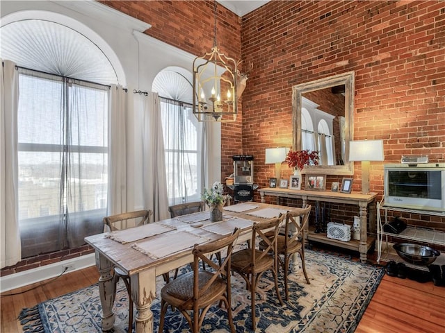 dining area featuring a chandelier, a towering ceiling, brick wall, and wood finished floors