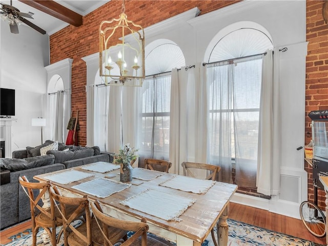 dining room featuring light wood-style floors, a wealth of natural light, beam ceiling, and brick wall