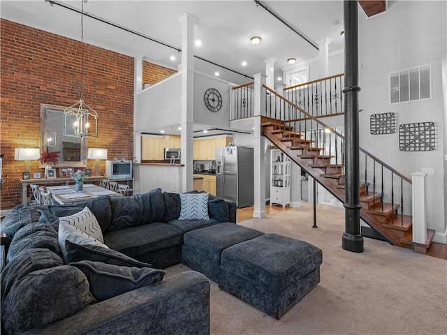 living room with decorative columns, visible vents, light colored carpet, a towering ceiling, and stairs