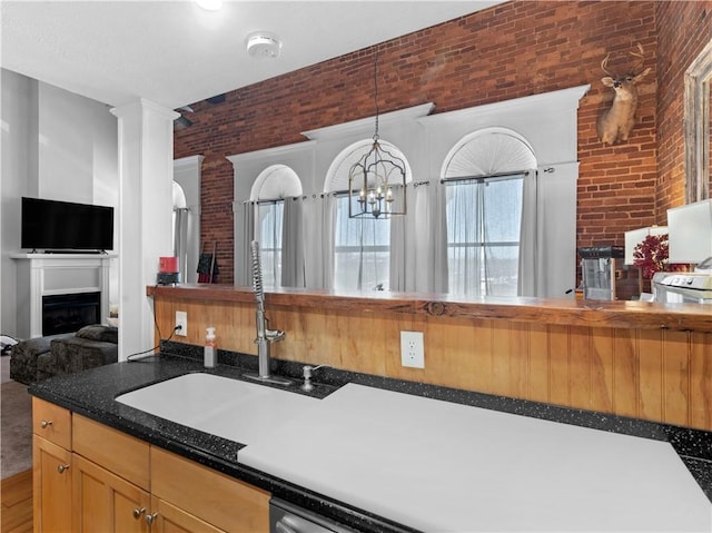 kitchen with decorative light fixtures, a fireplace, dark countertops, a sink, and brick wall