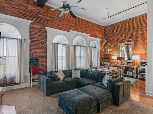 living area with brick wall, a high ceiling, a ceiling fan, and wood finished floors