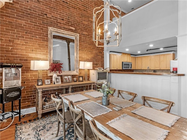 dining room featuring light wood-type flooring, brick wall, a towering ceiling, and a notable chandelier