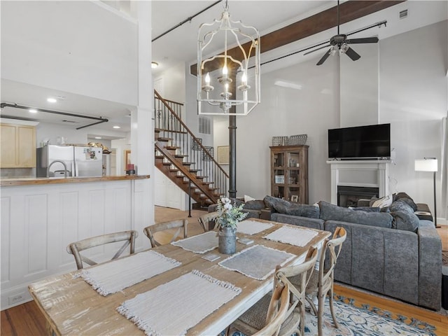 dining space with light wood-type flooring, high vaulted ceiling, a fireplace, and stairway