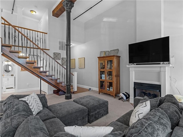 living area featuring light carpet, visible vents, a towering ceiling, stairs, and a fireplace