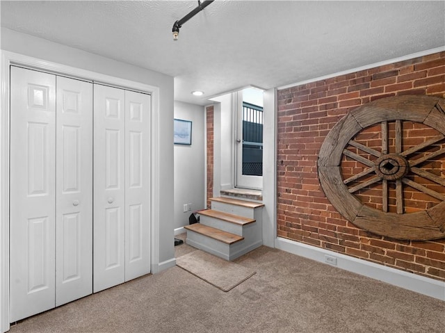 interior space with a textured ceiling, brick wall, carpet flooring, baseboards, and a closet