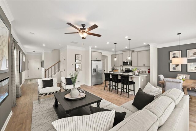 living room with ornamental molding, light hardwood / wood-style flooring, ceiling fan, and sink