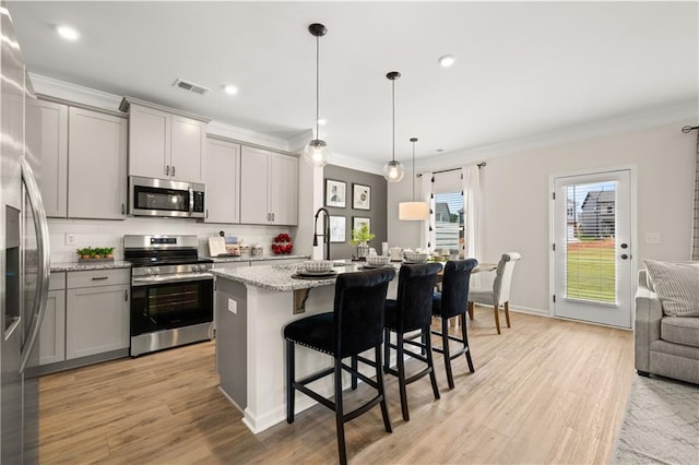 kitchen with appliances with stainless steel finishes, light stone countertops, a kitchen island with sink, gray cabinets, and pendant lighting