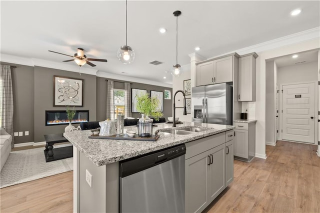 kitchen featuring stainless steel appliances, light hardwood / wood-style floors, decorative light fixtures, a kitchen island with sink, and gray cabinets