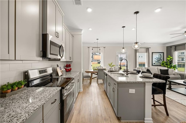 kitchen featuring stainless steel appliances, sink, decorative light fixtures, a kitchen island with sink, and light hardwood / wood-style flooring