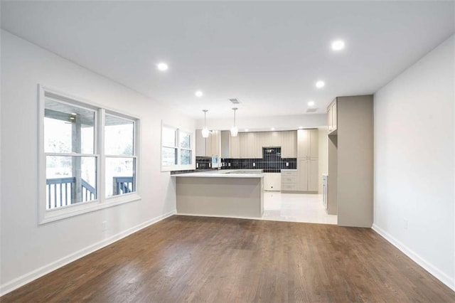 kitchen featuring hanging light fixtures, kitchen peninsula, dark wood-type flooring, a kitchen bar, and backsplash