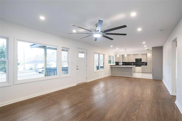 unfurnished living room featuring a healthy amount of sunlight, ceiling fan, and dark hardwood / wood-style floors