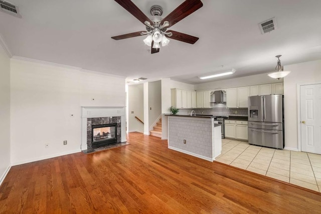 kitchen with hanging light fixtures, stainless steel appliances, white cabinets, wall chimney range hood, and backsplash