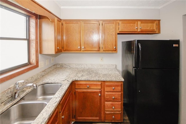 kitchen featuring freestanding refrigerator, a sink, light countertops, crown molding, and brown cabinetry