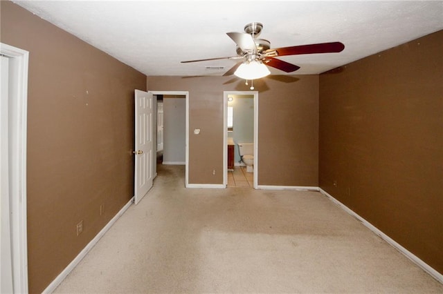 unfurnished bedroom with light colored carpet, baseboards, ensuite bathroom, and a ceiling fan