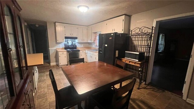 kitchen featuring tile patterned flooring, white cabinetry, black refrigerator, and electric stove