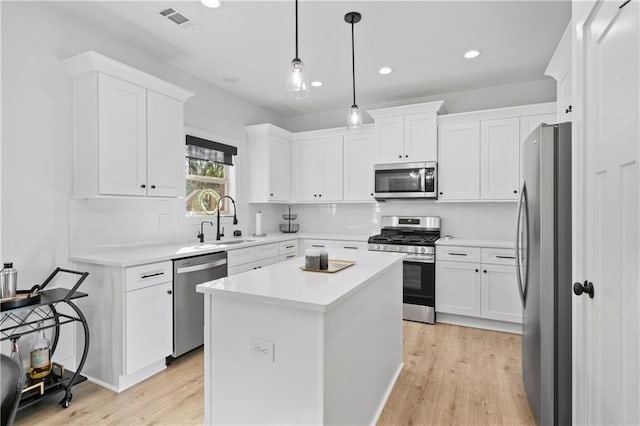 kitchen with white cabinets, a kitchen island, decorative light fixtures, stainless steel appliances, and sink