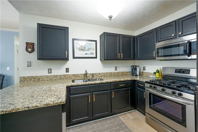 2305 Keenland Ct, Cumming, GA 30040 - kitchen featuring appliances with stainless steel finishes, a sink, light wood-type flooring, a peninsula, and a textured ceiling