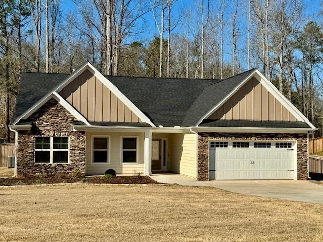 craftsman house featuring board and batten siding, concrete driveway, a front yard, a garage, and stone siding