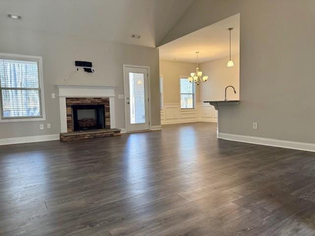 unfurnished living room with visible vents, a notable chandelier, a fireplace, dark wood-style flooring, and vaulted ceiling