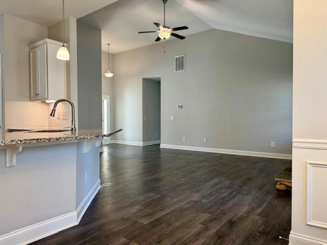 kitchen with visible vents, a ceiling fan, light stone counters, a breakfast bar area, and white cabinets