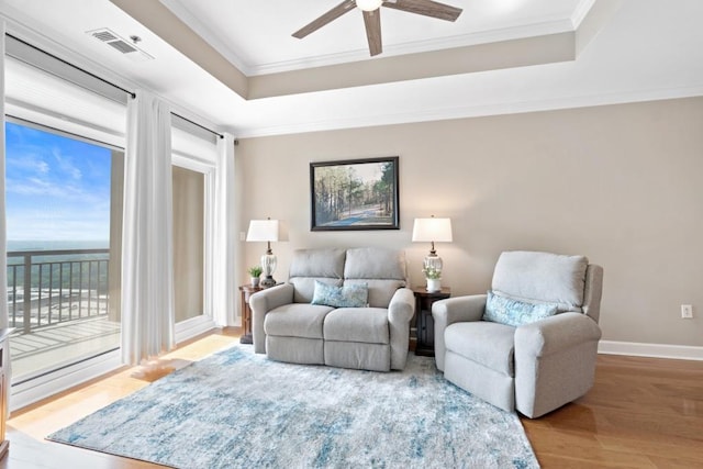 living room with ornamental molding, a ceiling fan, wood finished floors, a raised ceiling, and baseboards
