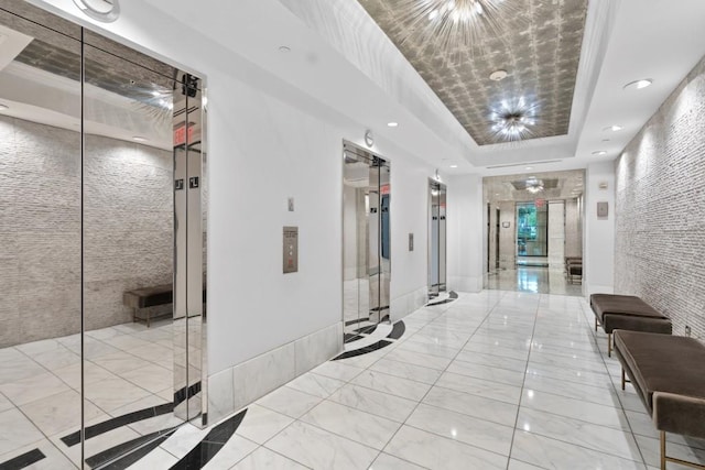 hall featuring a raised ceiling, marble finish flooring, elevator, and recessed lighting