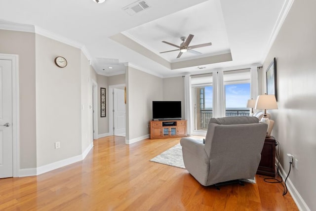 living area with a tray ceiling, light wood finished floors, a ceiling fan, ornamental molding, and baseboards