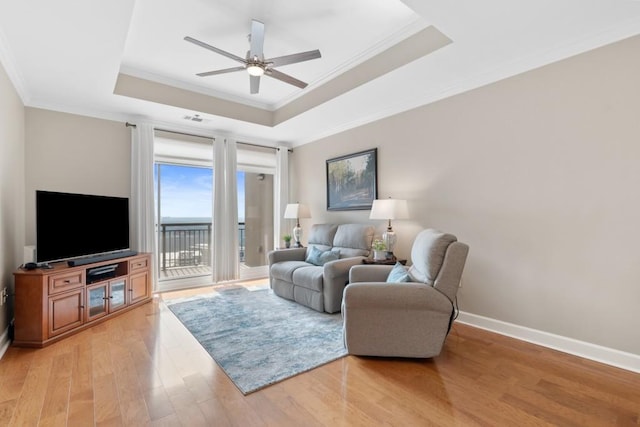 living area with a tray ceiling, ornamental molding, a ceiling fan, light wood-style floors, and baseboards