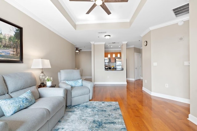 living area featuring a ceiling fan, wood finished floors, a tray ceiling, crown molding, and baseboards