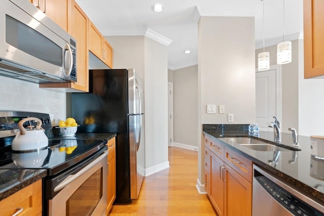 kitchen featuring stainless steel appliances, a sink, light wood-style flooring, dark stone countertops, and ornamental molding